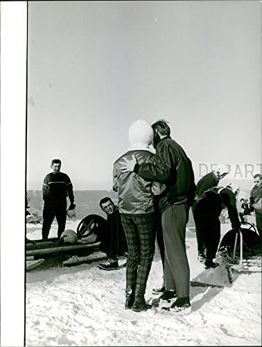 תצלום וינטג 'של הצד האחורי של בריג'יט ברדו עומד על גבעה מושלגת עם אנשים.